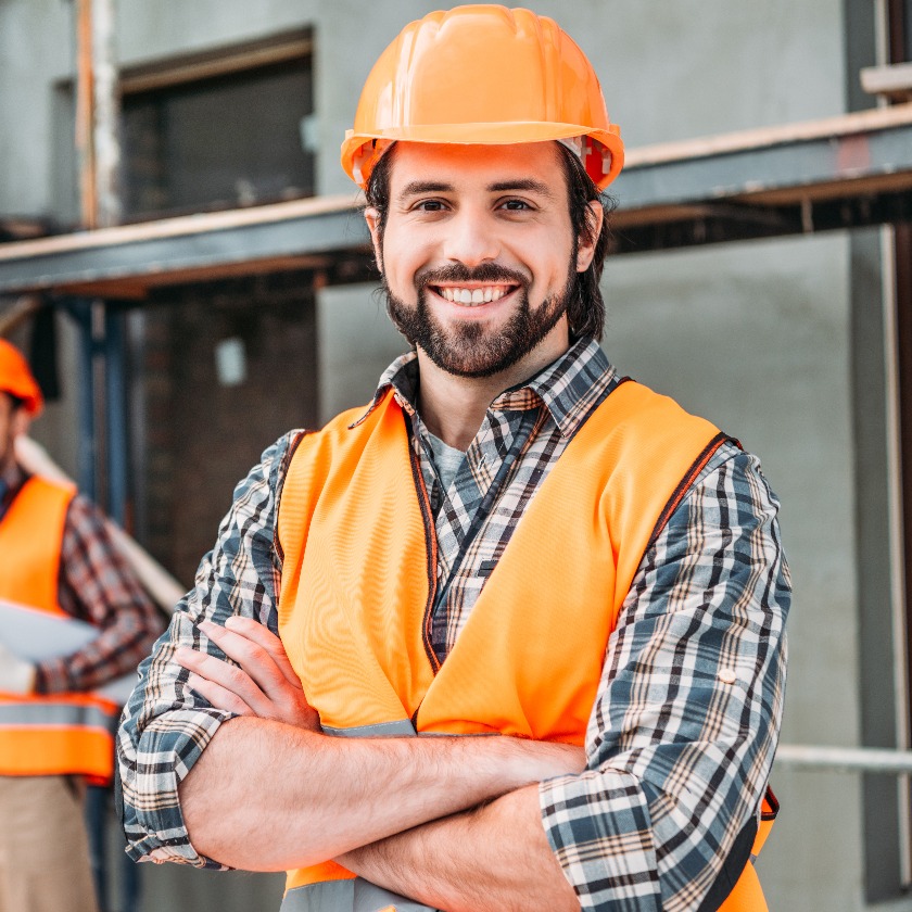 Gut aussehender, lächelnder Bauarbeiter auf der Baustelle mit Krückstock